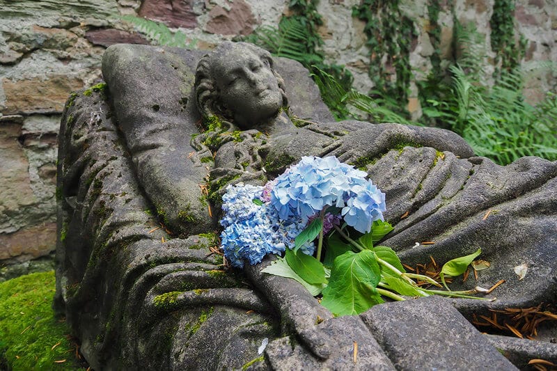 Carolines sculpted tomb with bright blue flowers near her arm