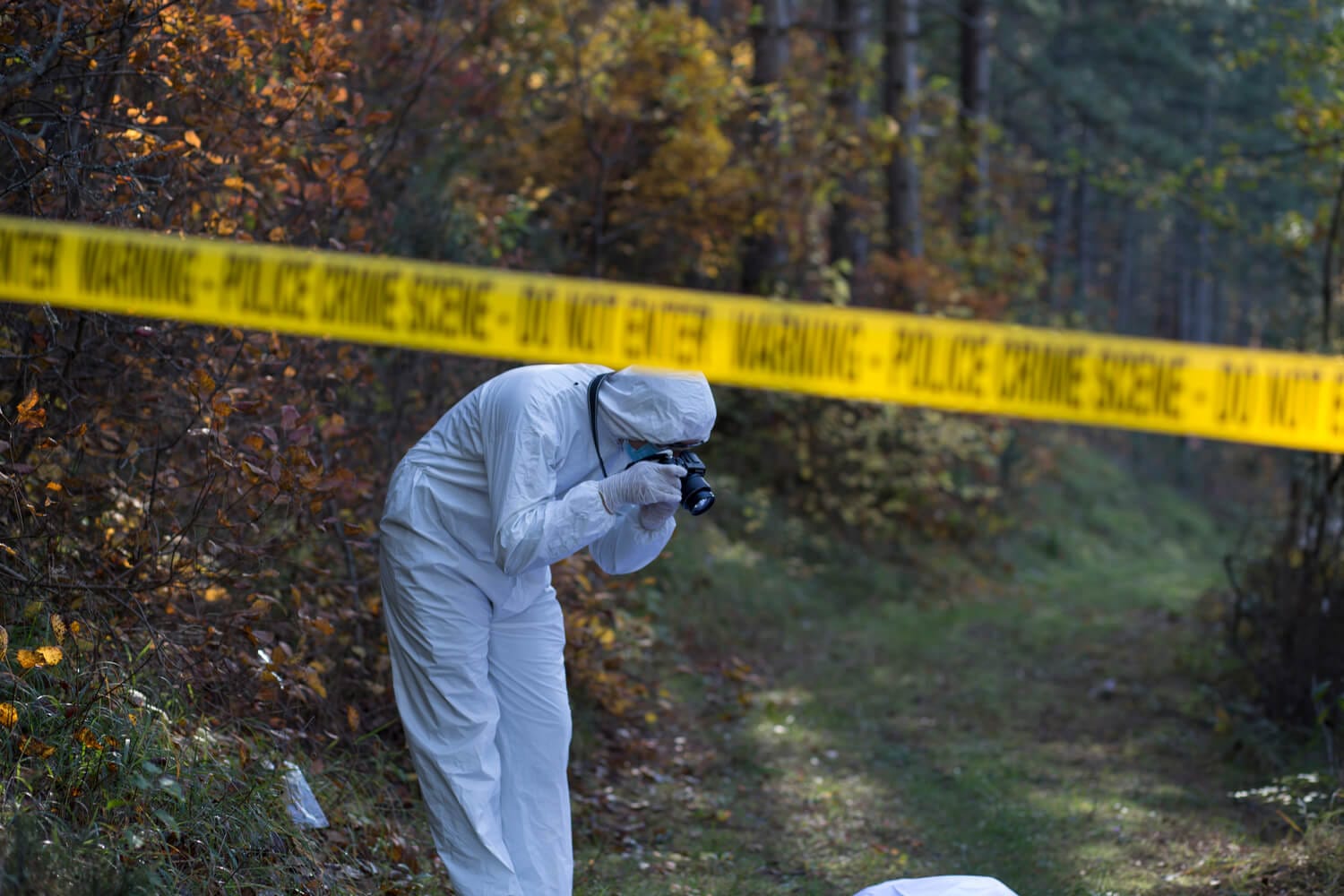 A forensic officer dressed in a white hazmat suit, taking photos of the crime scene